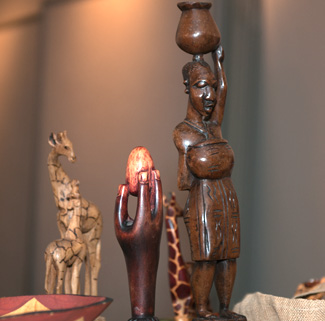 Carved wooden statues of two giraffes, a hand holding an egg, and a woman holding a water vessel on her head